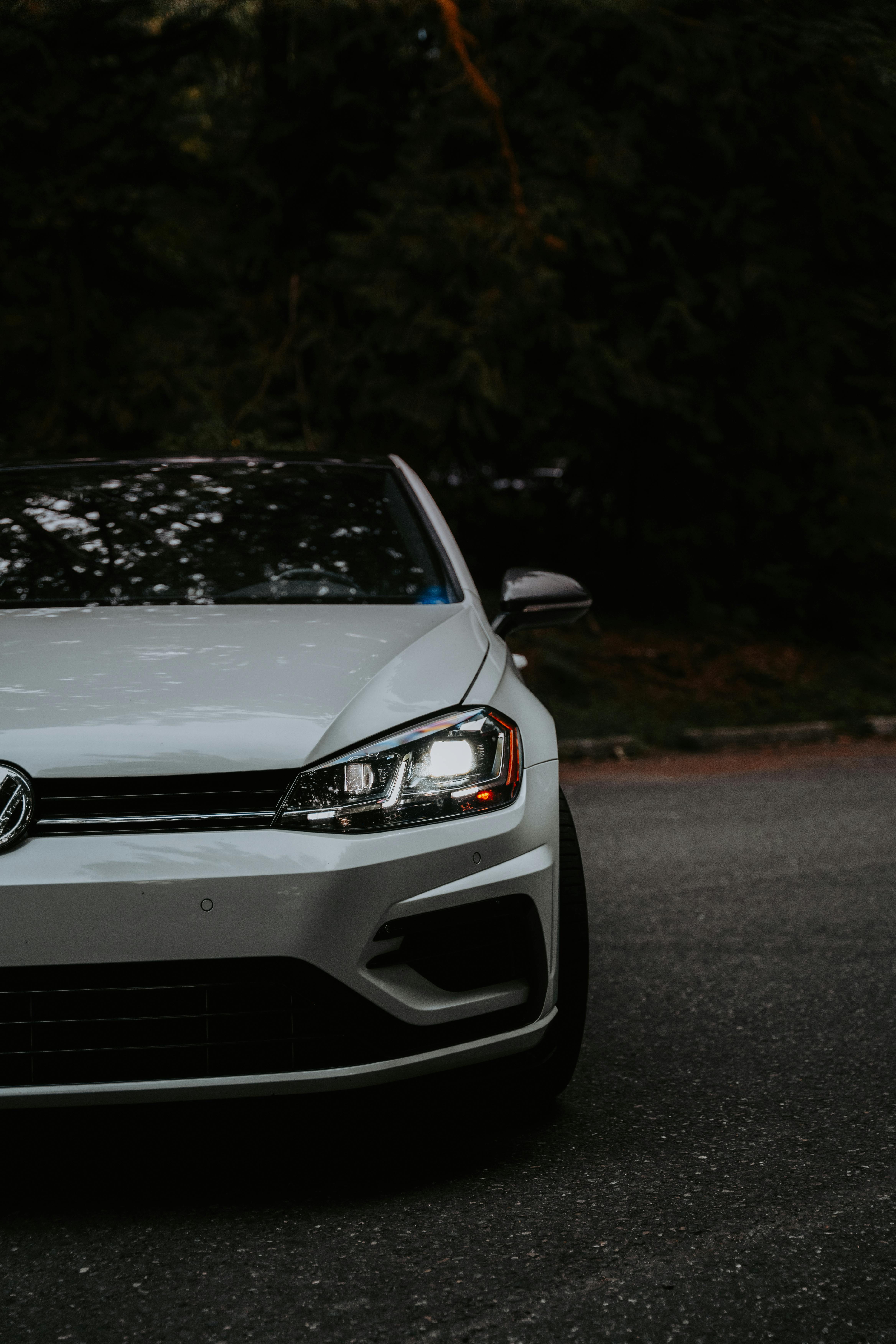 Half of a front facing white VW Golf with dark road behind it.