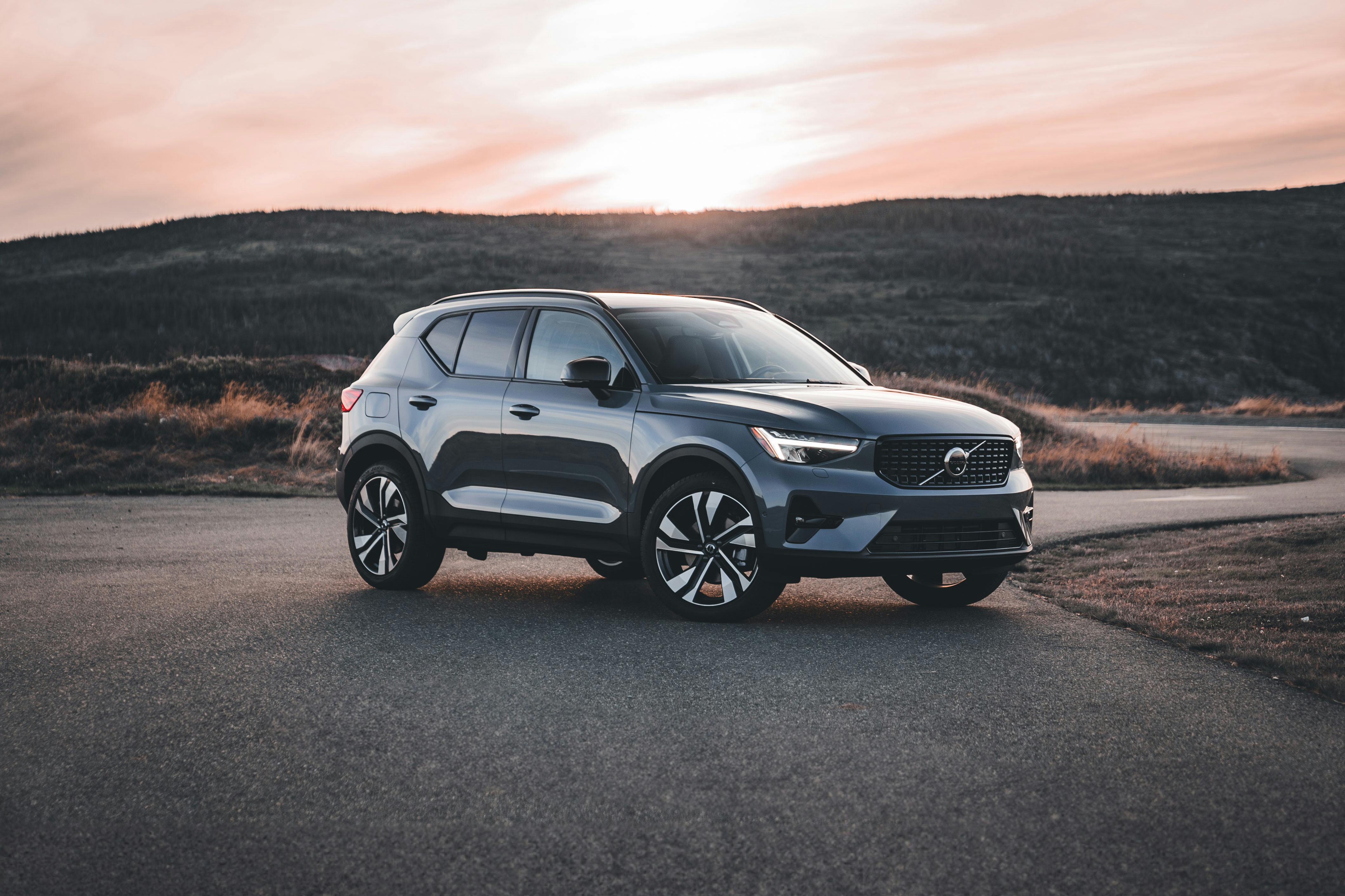 Blue Volvo XC40 on empty countryside road with sun setting behind it